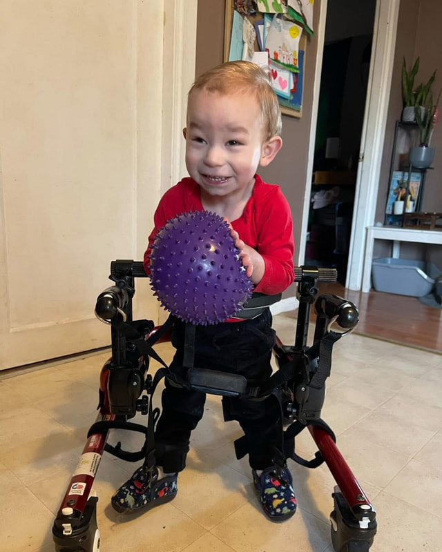 A smiling child holding a purple sensory ball